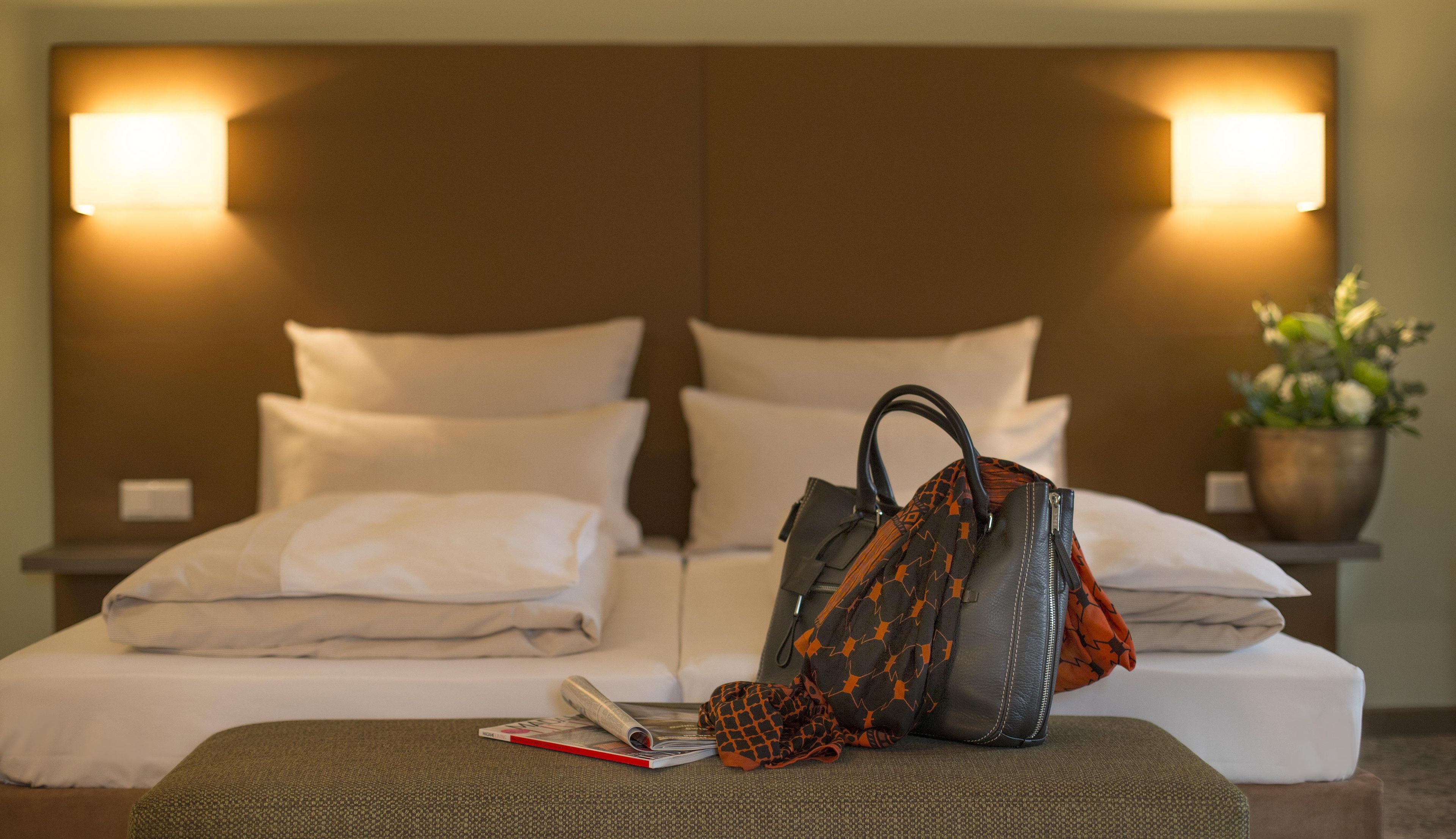 Un lit bien fait, avec des oreillers, un sac à main et un magazine posés sur une table de chevet.