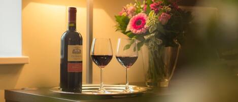 A bottle of wine, two wine glasses, a lamp, and a vase with flowers on a table.