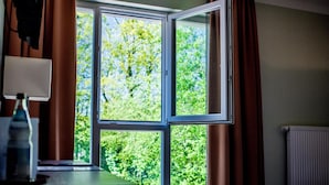 A room with a large window, a radiator, and a lamp on a table. - Hotel Jakob Regensburg DownTown, BW Signature Collection (Regensburg)