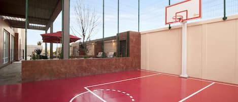 An outdoor basketball court with a red surface, a basketball hoop, and a fence.