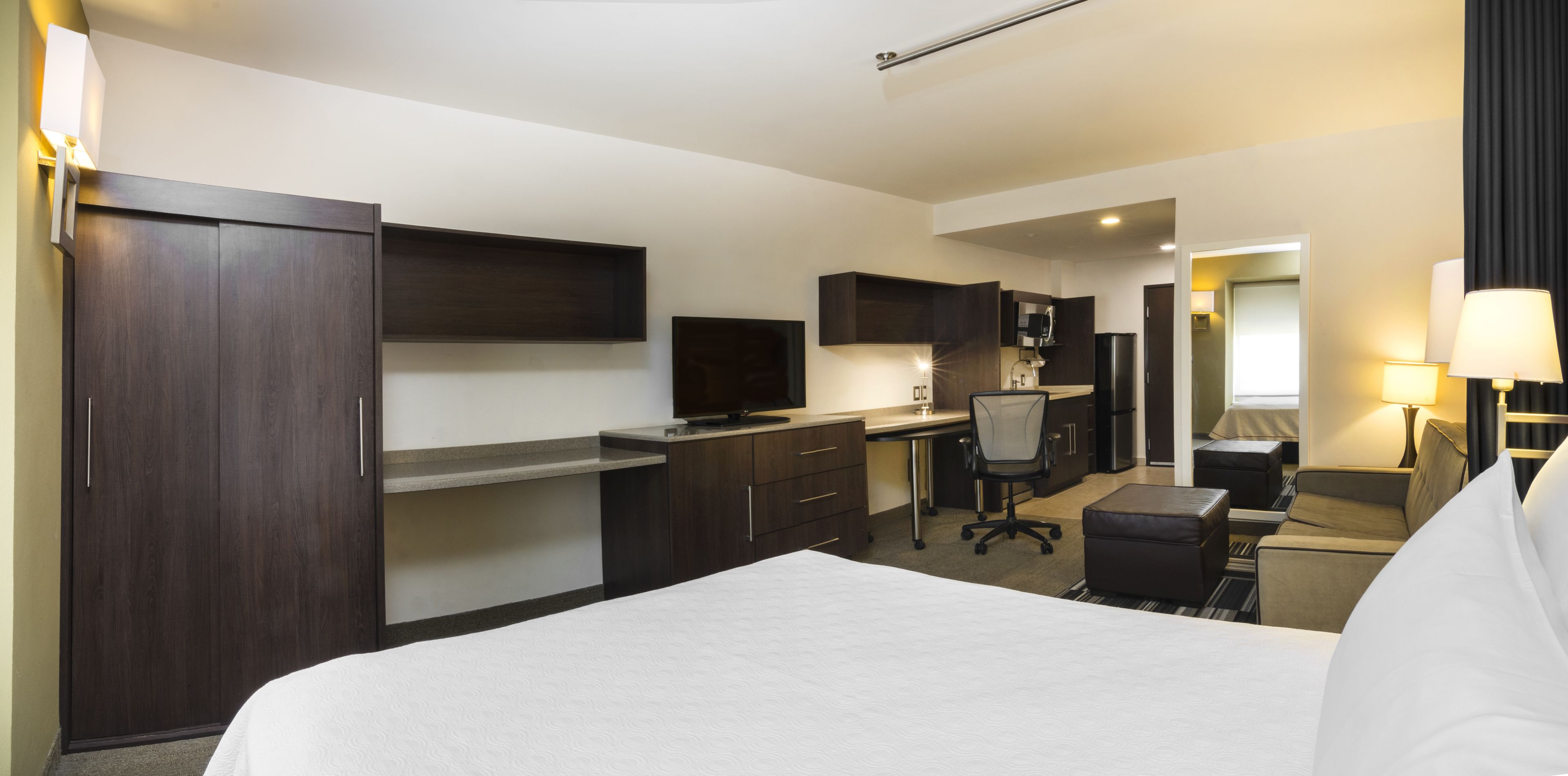 A hotel room with a bed, a desk, a chair, a sofa, and a TV.