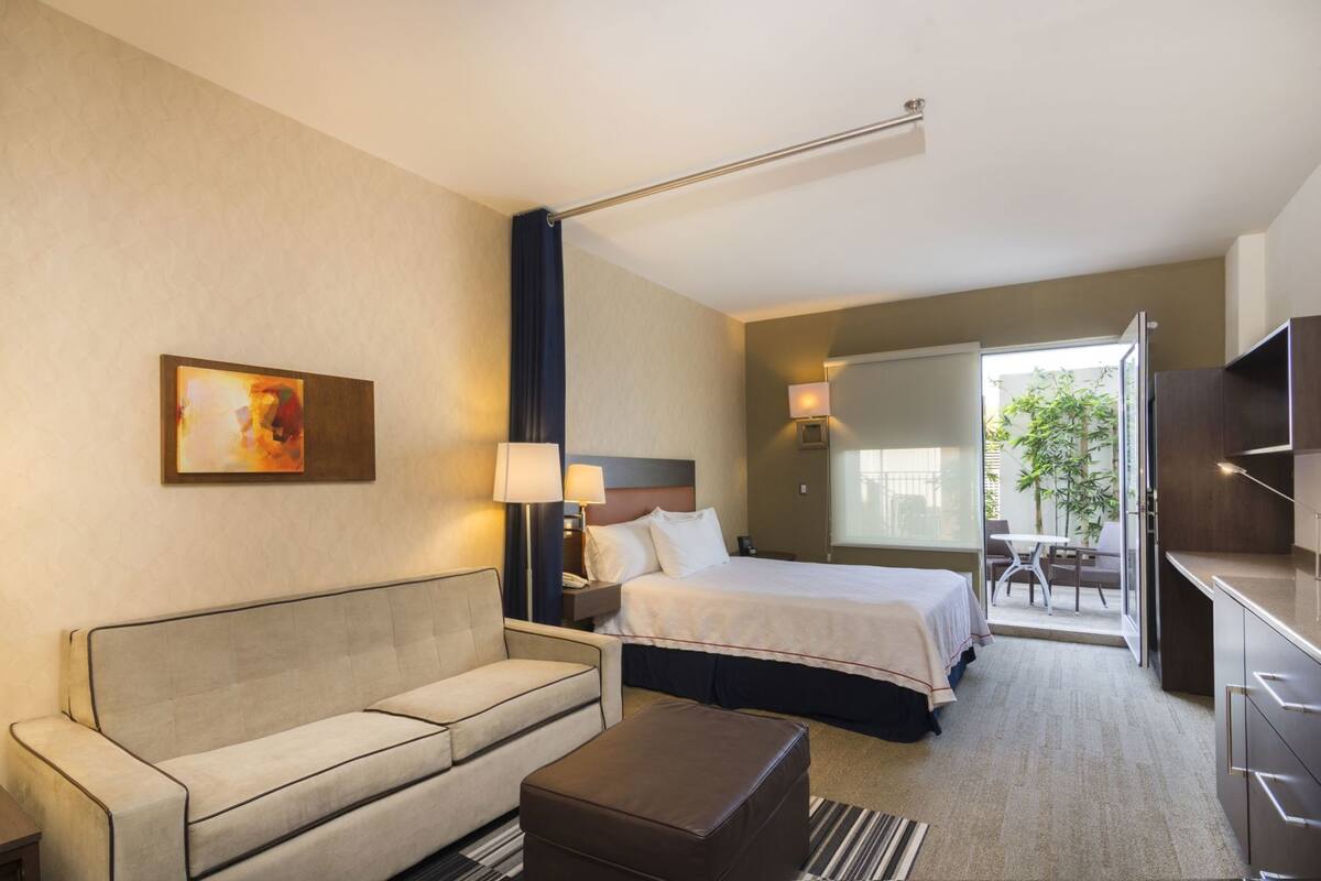 A hotel room with a bed, a sofa, a coffee table, a TV, and a painting on the wall.