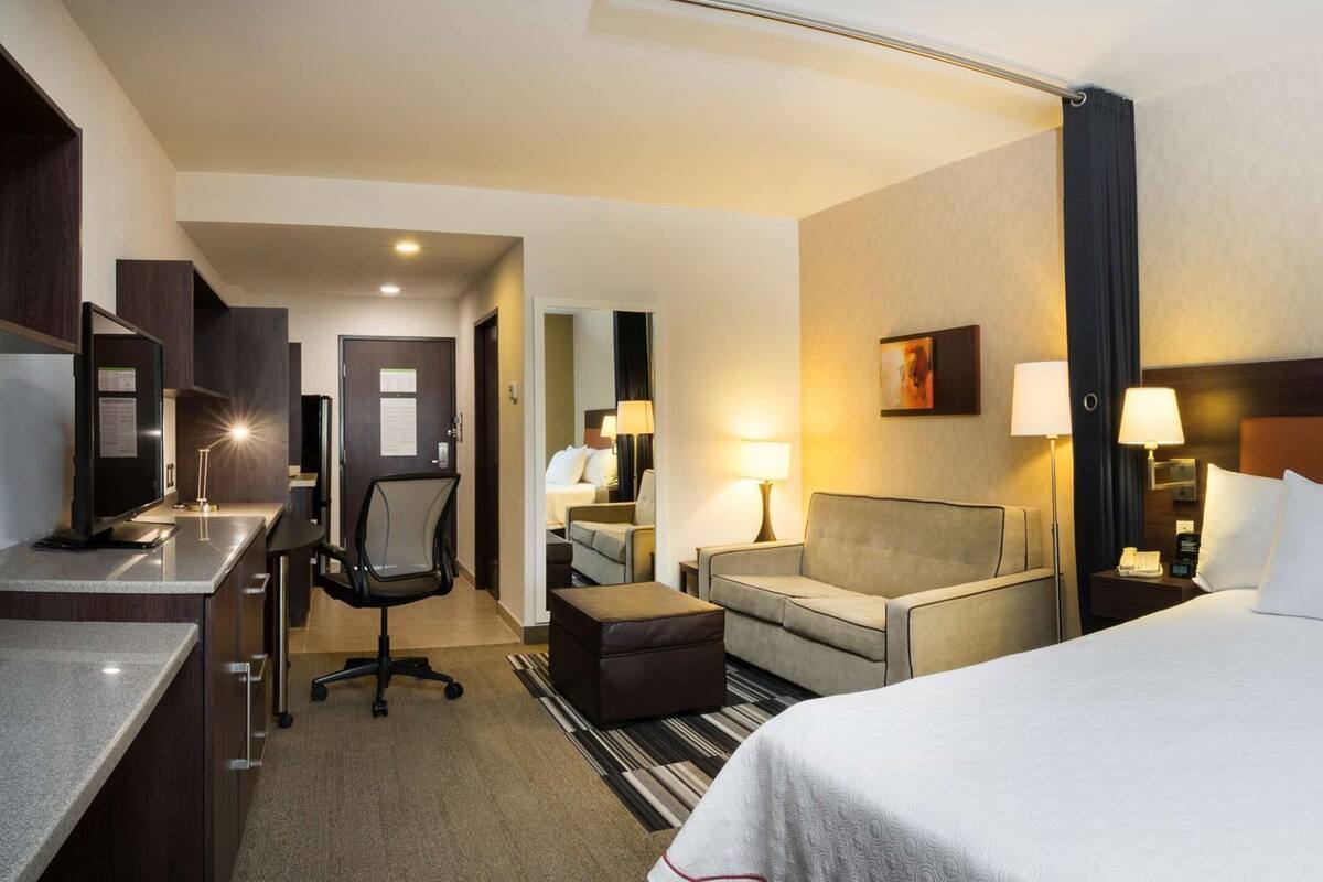 A hotel room with a bed, a desk, a chair, a sofa, and a small table.