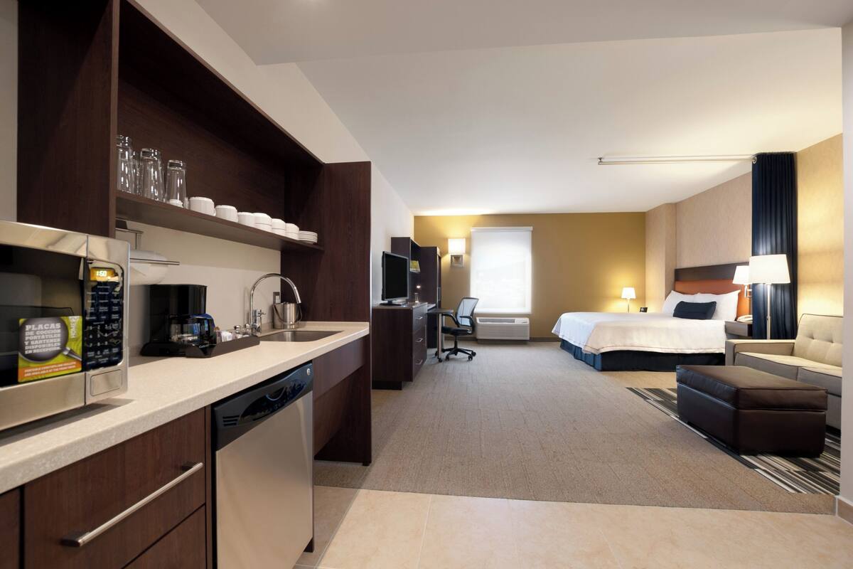 A hotel room with a kitchenette, a bed, a desk, and a seating area.