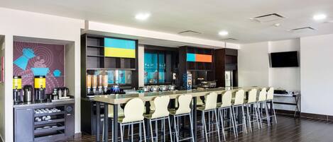 Una zona de bar moderna con una barra alargada, taburetes y una variedad de bebidas.