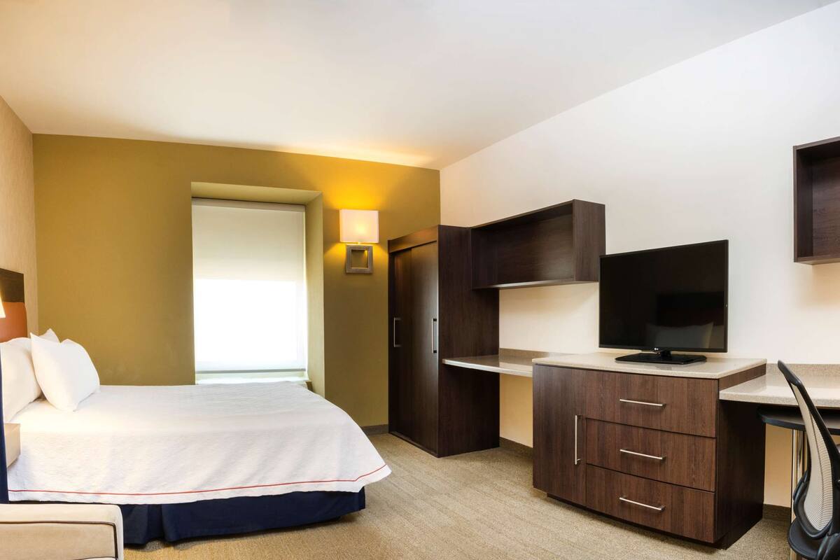 A hotel room with a bed, desk, chair, and a TV.