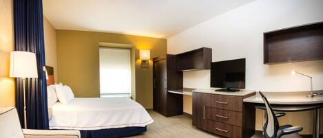 A hotel room with a bed, desk, chair, and a TV.