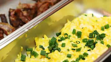A buffet with scrambled eggs garnished with chives and a separate section with bacon.