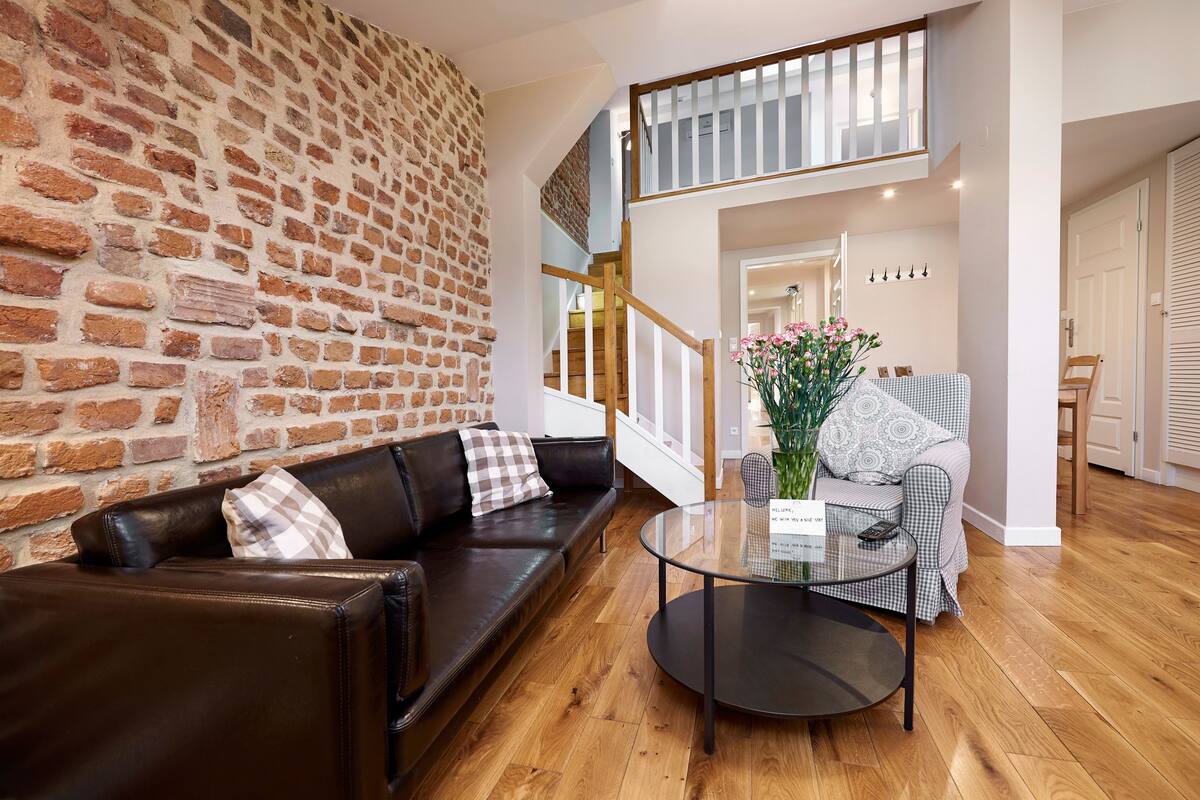 Un salon moderne avec un mur en briques, un canapé en cuir et une table basse en verre.