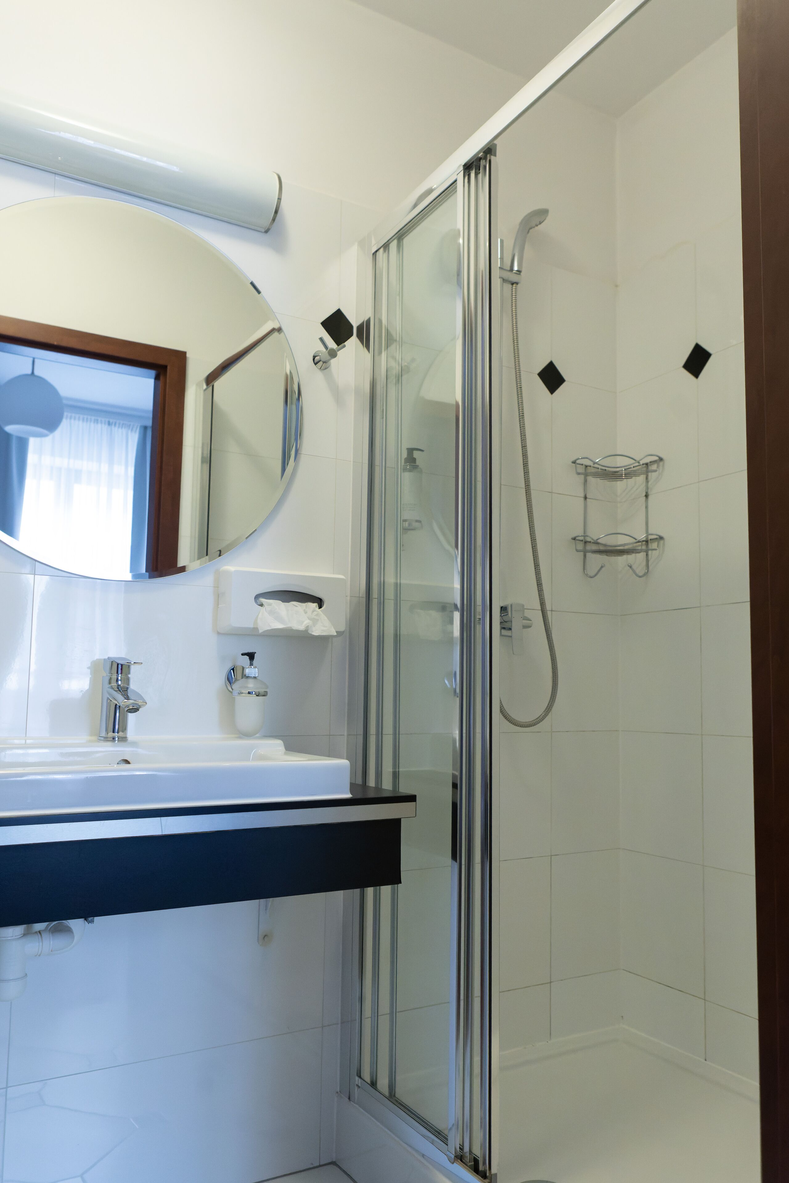 A modern bathroom with a glass-enclosed shower, a sink with a mirror above, and a towel dispenser.
