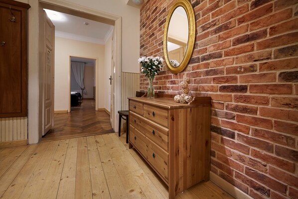 A hallway with a wooden floor, a wooden dresser, a mirror, and a brick wall. - Gołębia 8 Residence (Kraków)