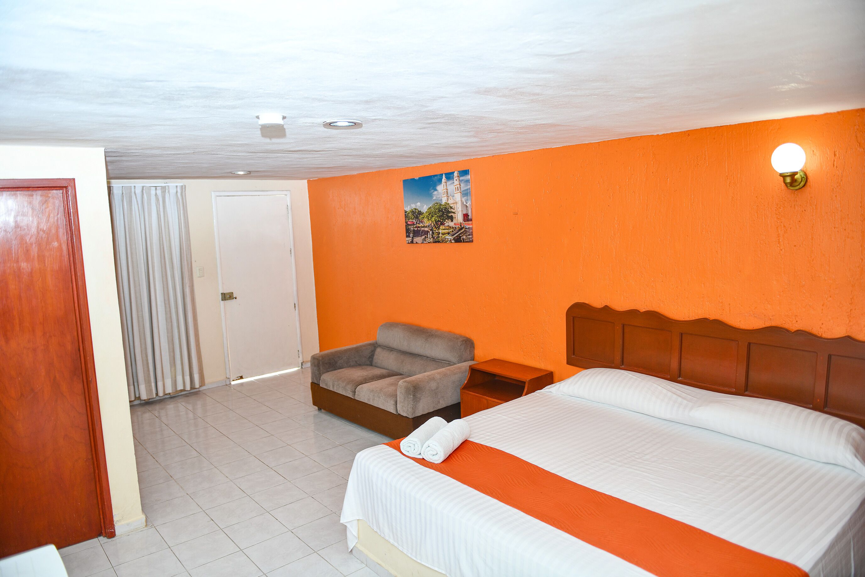 A hotel room with a bed, a chair, a nightstand, and a picture on the wall.