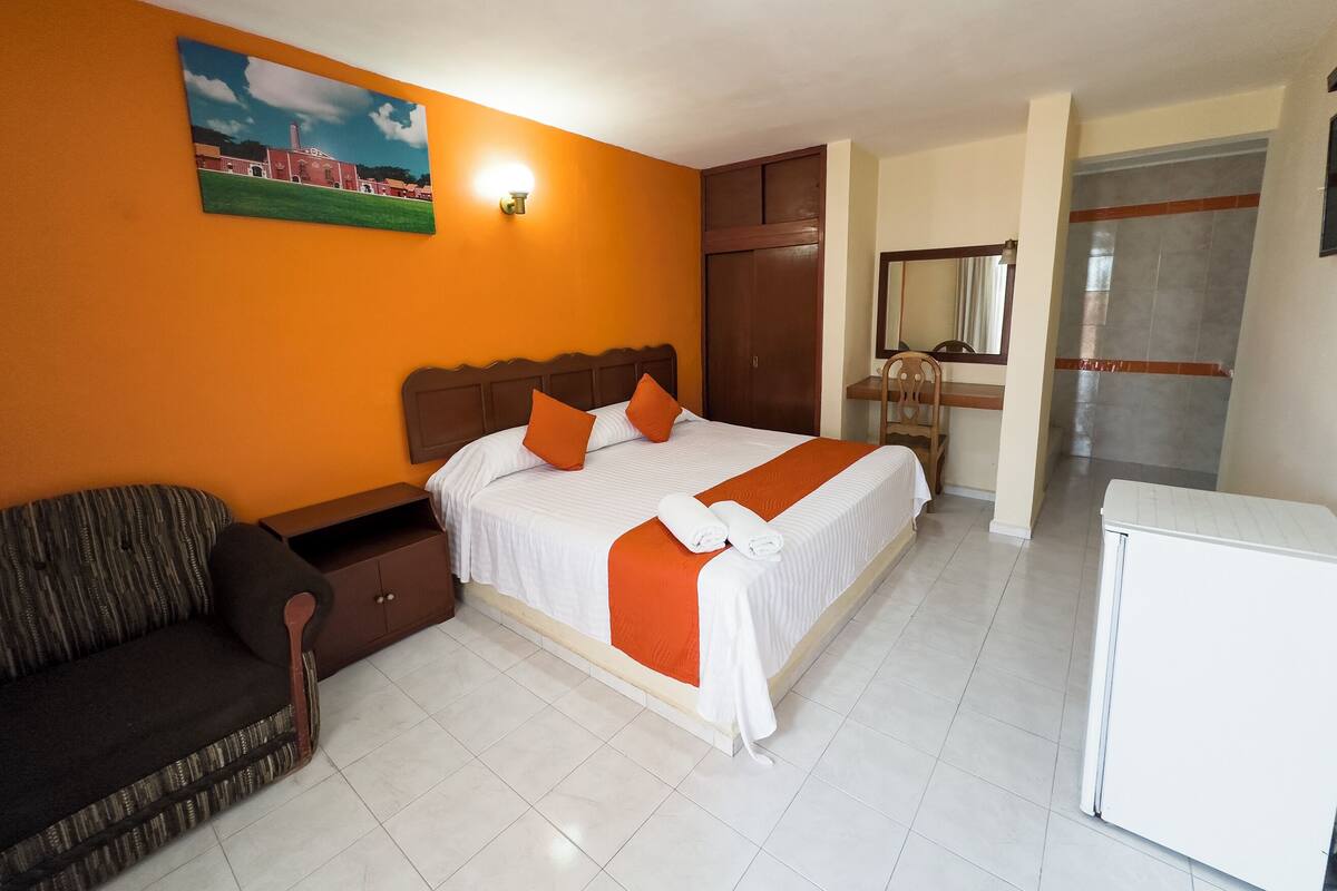 Una habitación de hotel con cama, escritorio, sillón, sofá y un cuadro en la pared.