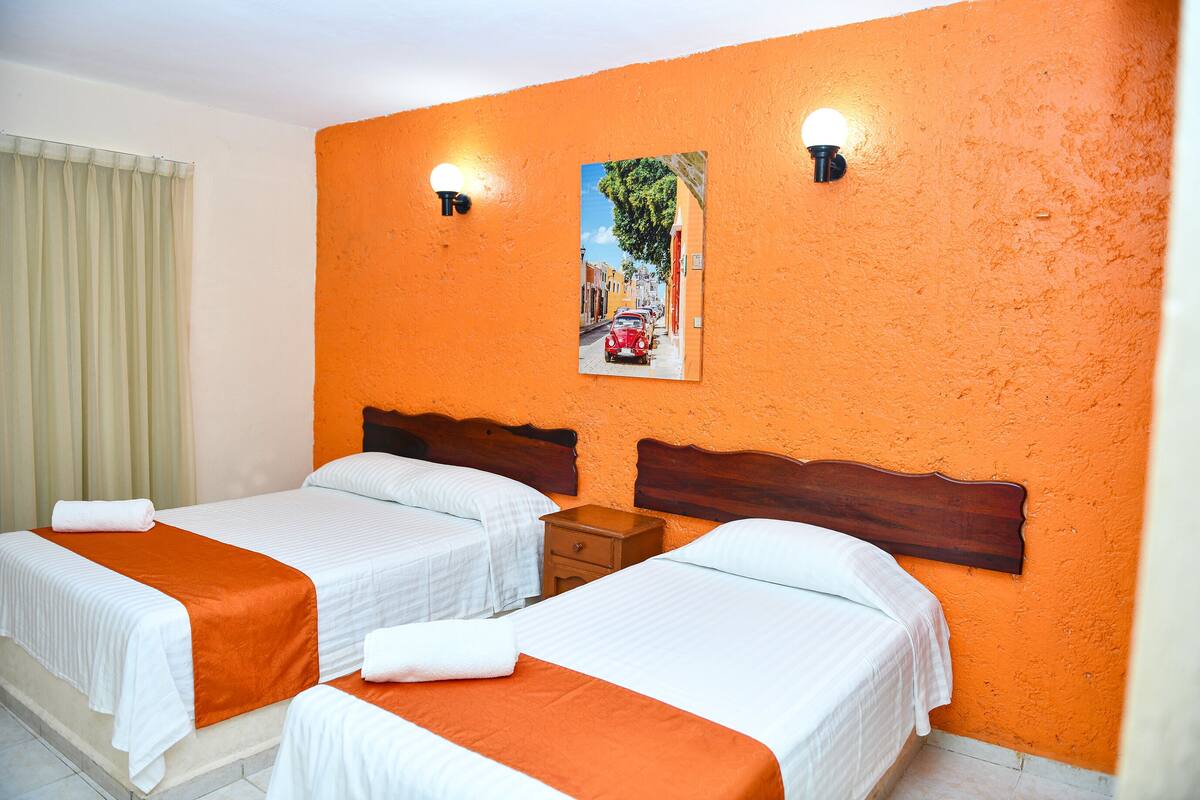 Habitación de hotel con dos camas, una mesita de noche y un cuadro colgado en la pared.