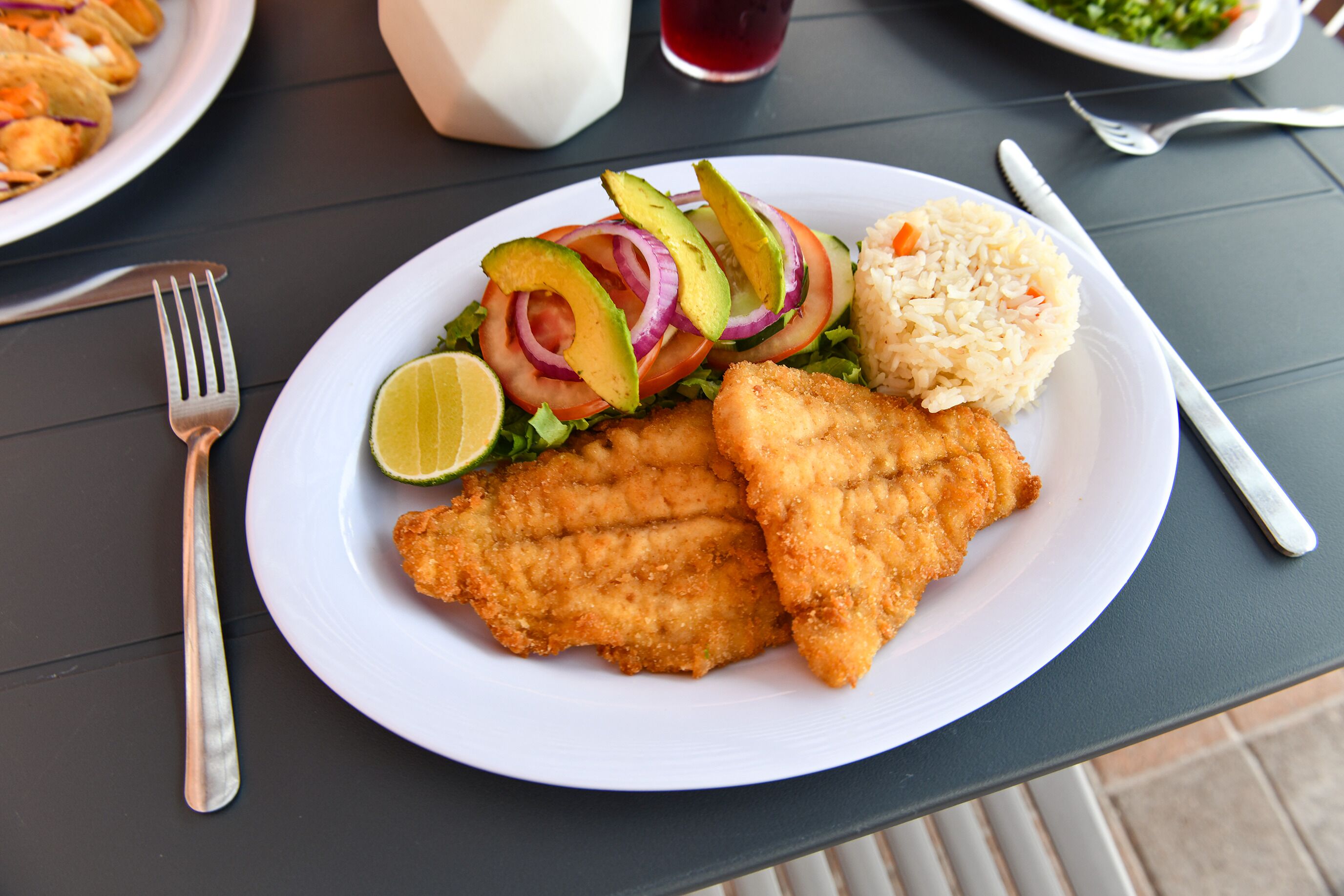 Un plato con un filete de pescado empanizado, ensalada y arroz.