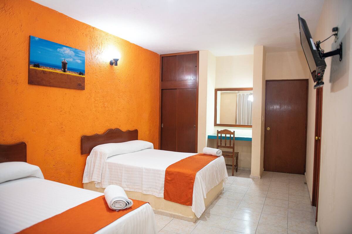 Una habitación de hotel con dos camas, un cuadro que representa una playa, un armario de madera, un escritorio con una silla y un televisor fijado a la pared.
