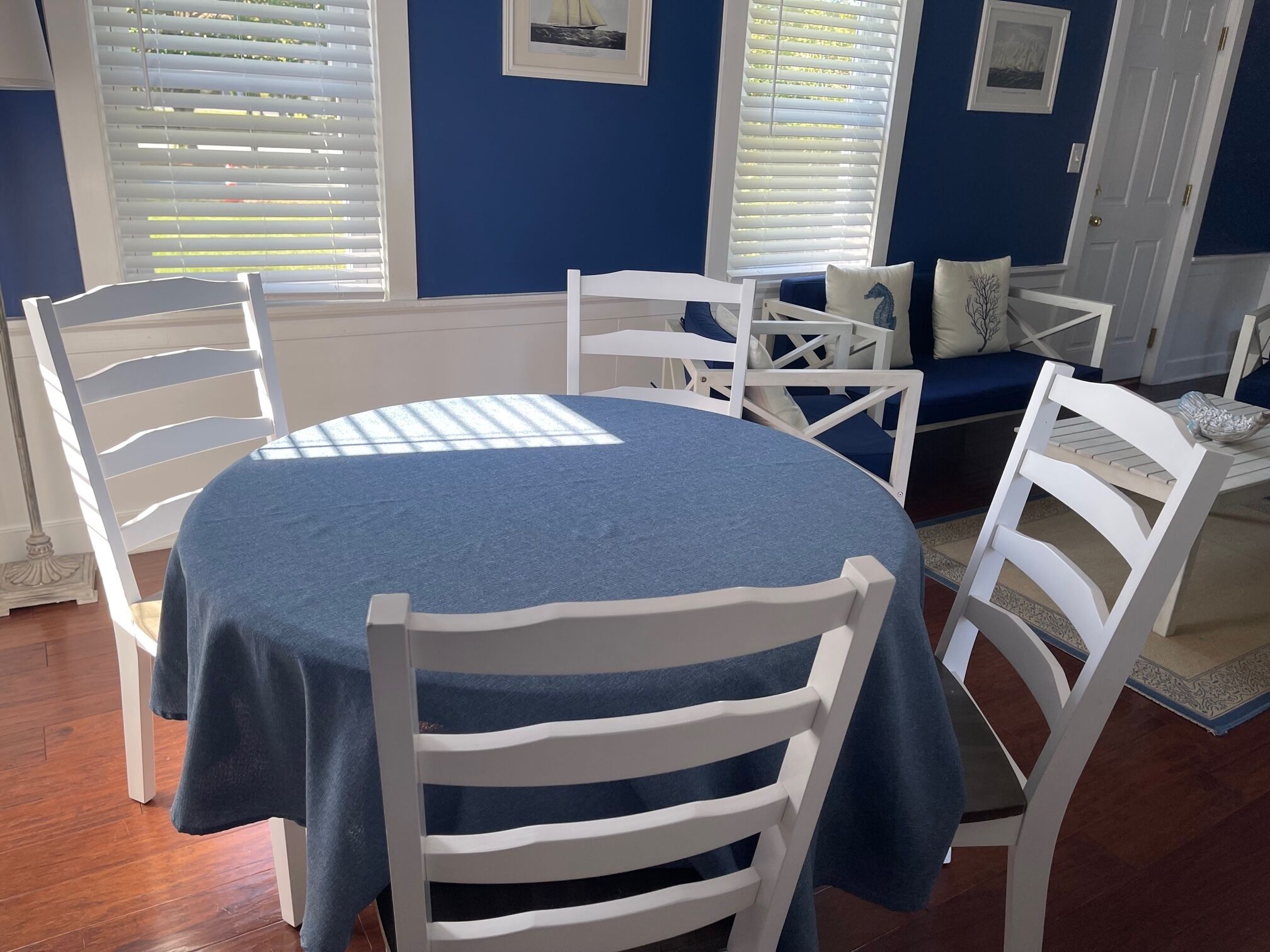 Un espace repas avec une table ronde recouverte d’une nappe bleue, entourée de chaises blanches.