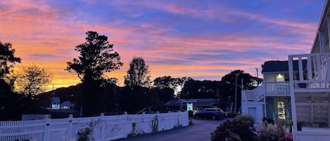 A sunset view from a hotel with a white fence, outdoor seating, and a building with a balcony.