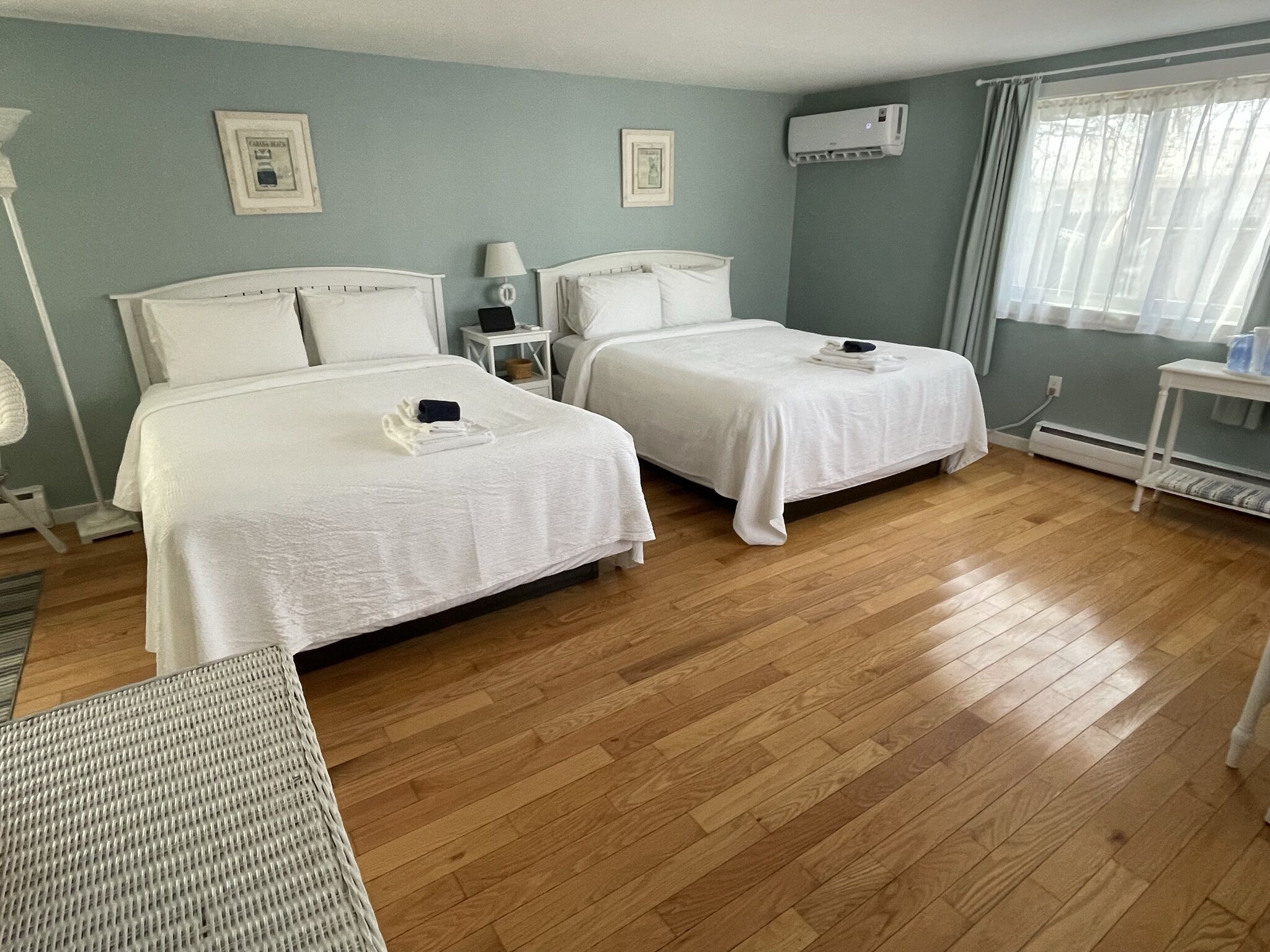 Une chambre d’hôtel avec deux lits, un radiateur mobile, une petite table et une fenêtre avec des rideaux.
