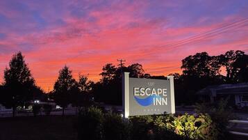 Señal del Hotel Escape Inn con una vista despejada del entorno, incluyendo árboles y líneas eléctricas.