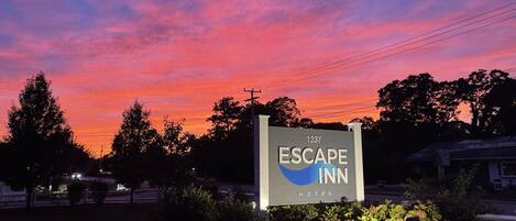 A sign for Escape Inn Hotel with a clear view of the surrounding area, including trees and power lines.