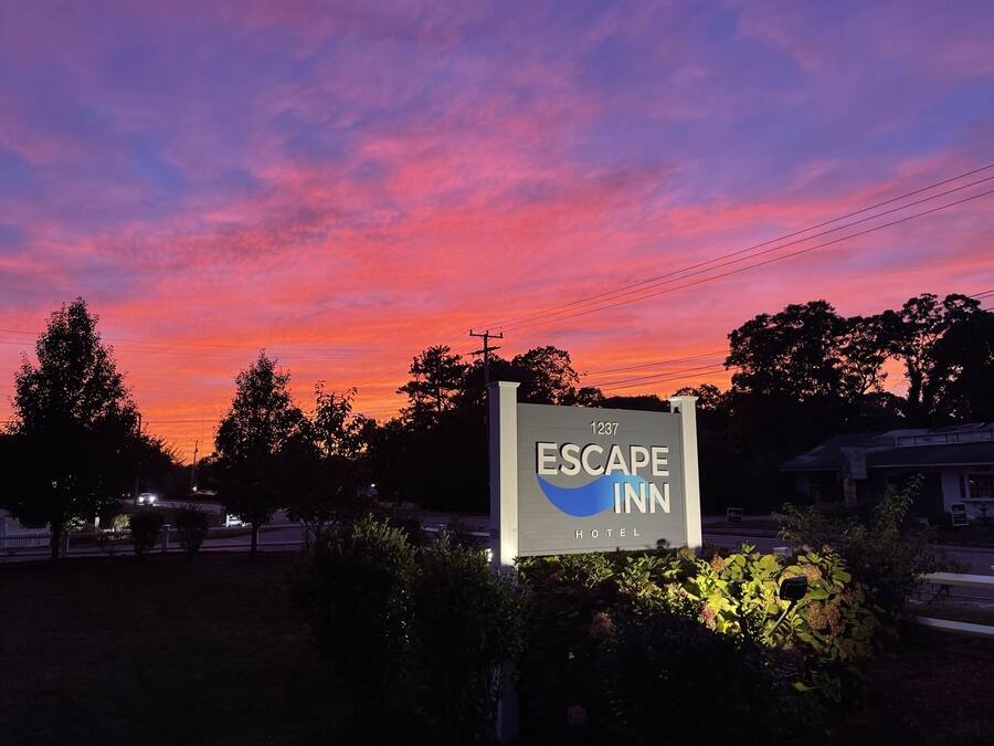 Schild des Escape Inn Hotels mit freiem Blick auf die Umgebung, darunter Bäume und Stromleitungen.