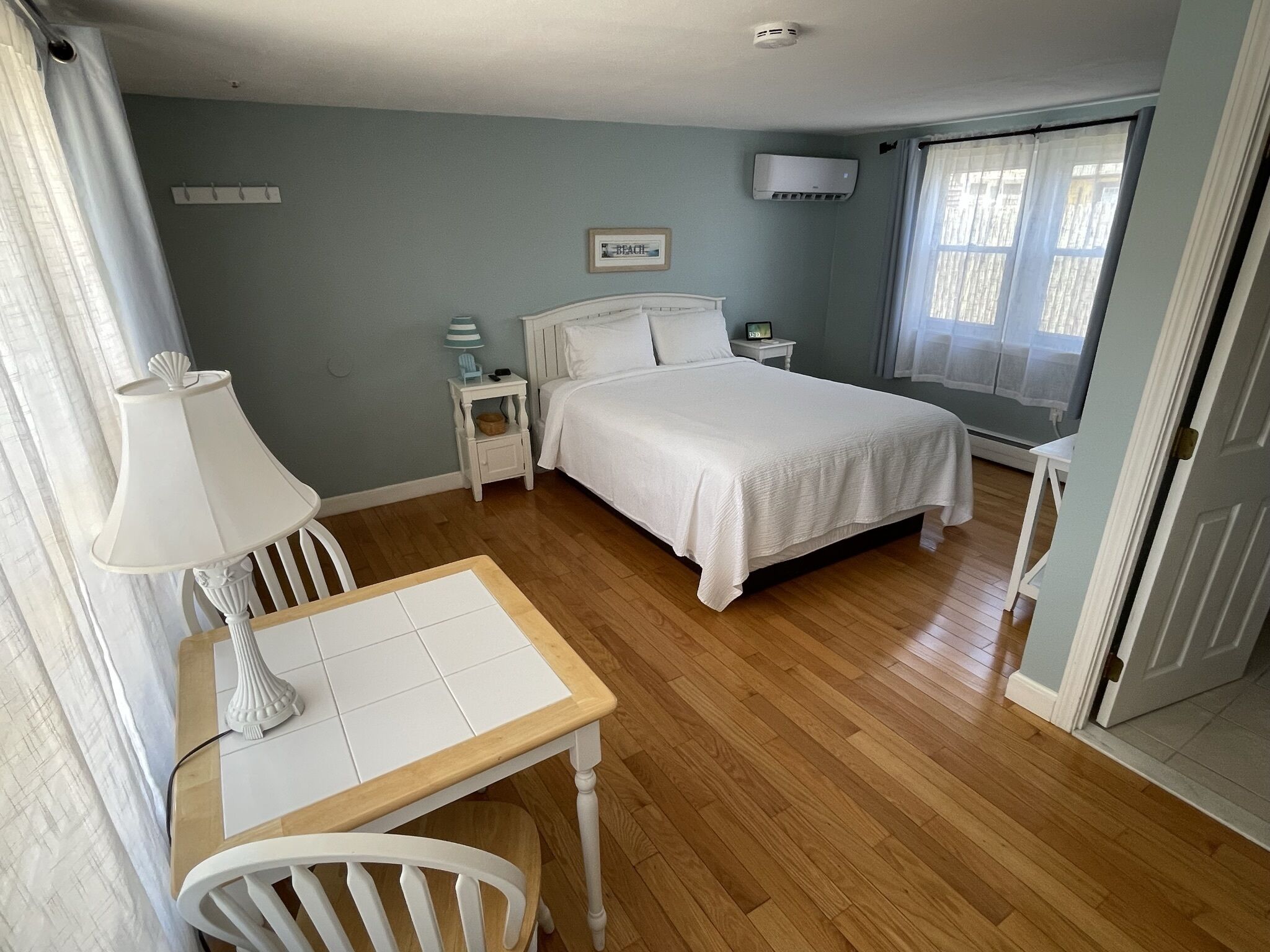 Un dormitorio con cama, mesitas de noche, lámpara, silla y ventana.