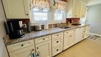 A kitchen with white cabinets, granite countertops, a coffee maker, a toaster, and a hanging fish decoration.