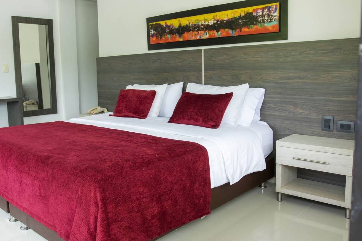 Een hotelkamer met een groot bed, een bureau, een stoel, een spiegel en een schilderij aan de muur.