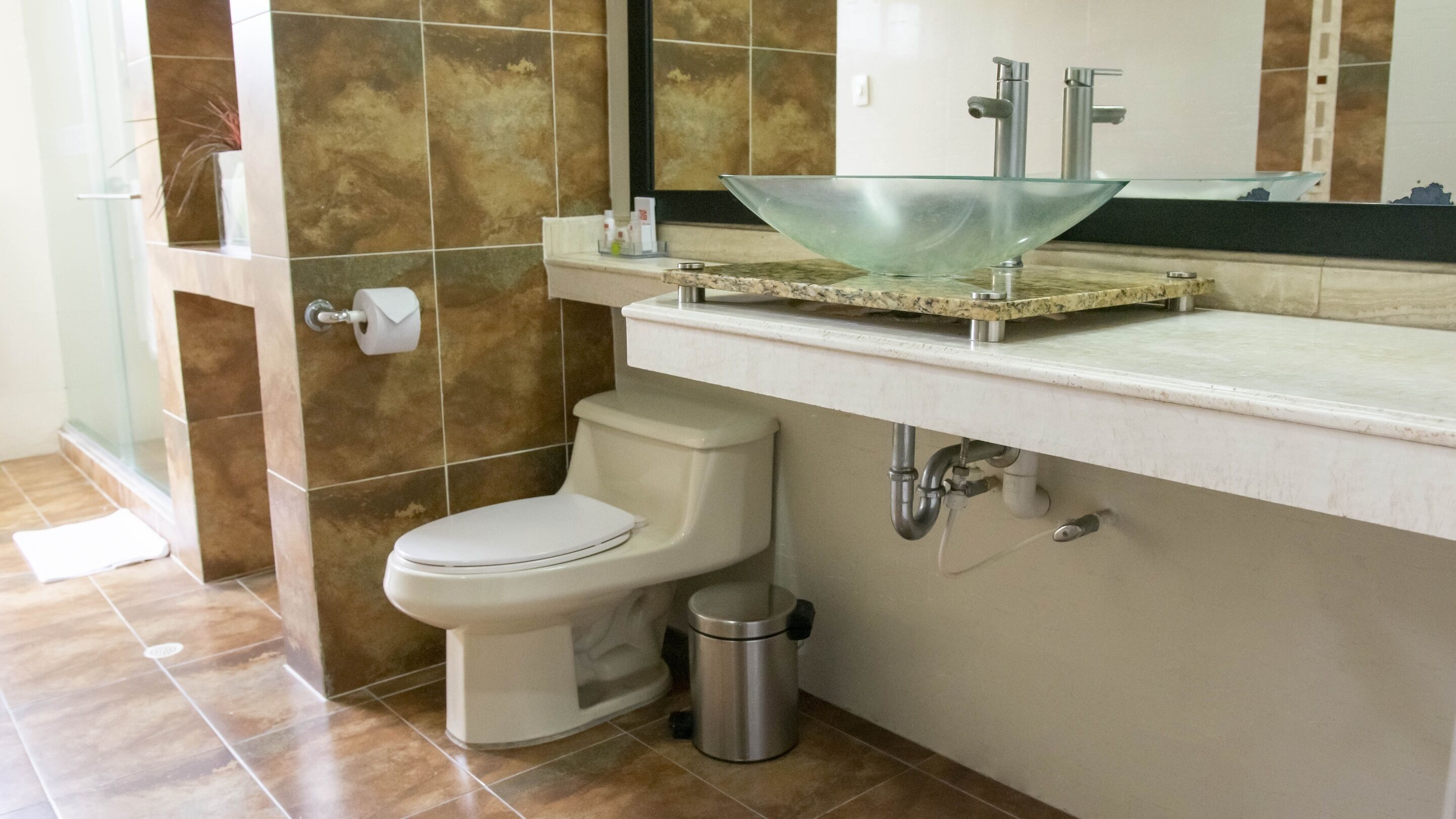 A modern bathroom with a glass sink, toilet, and shower area.