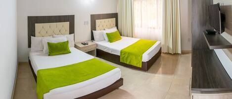 Habitación de hotel con dos camas, cada una con una manta verde, un cabecero de madera y una mesita de noche con un teléfono.