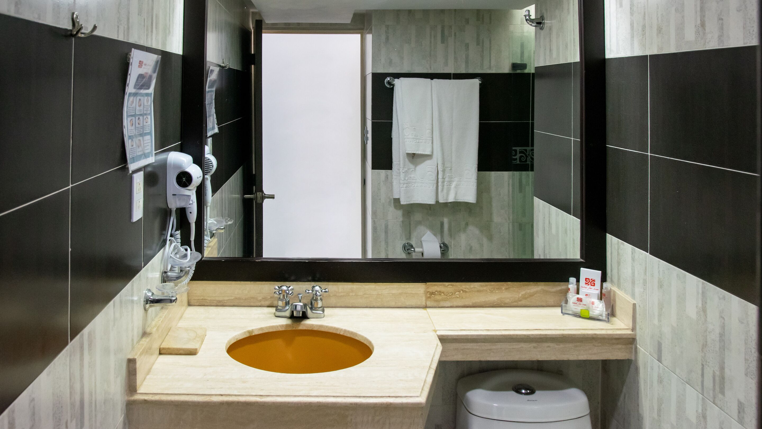 Un baño moderno con un lavabo color beige, un secador de pelo sujeto a la pared y un inodoro.
