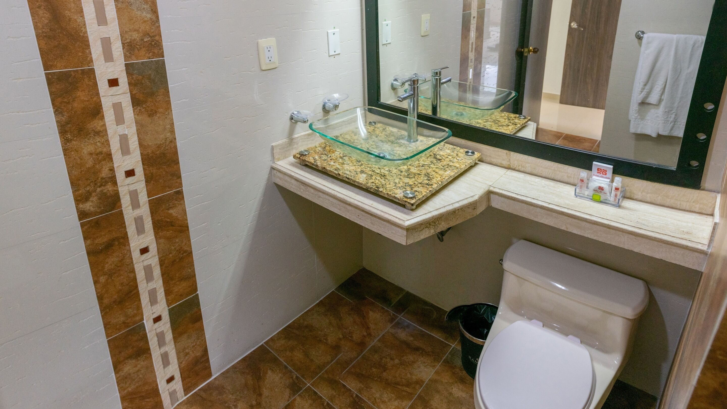 A bathroom with a glass sink, a white toilet, and a trash can.