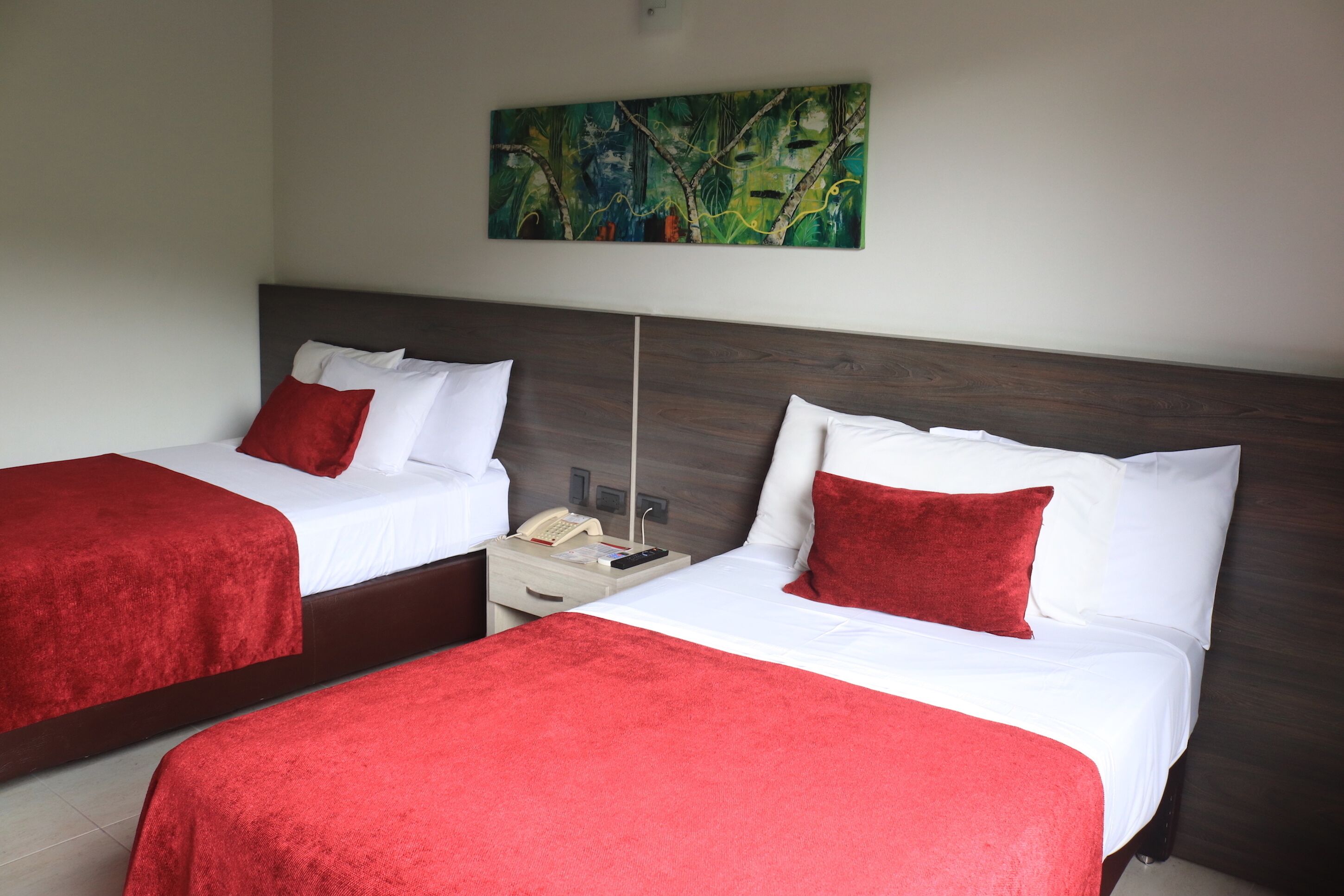 Two single beds with red bedding, a nightstand with a telephone, and a painting on the wall.