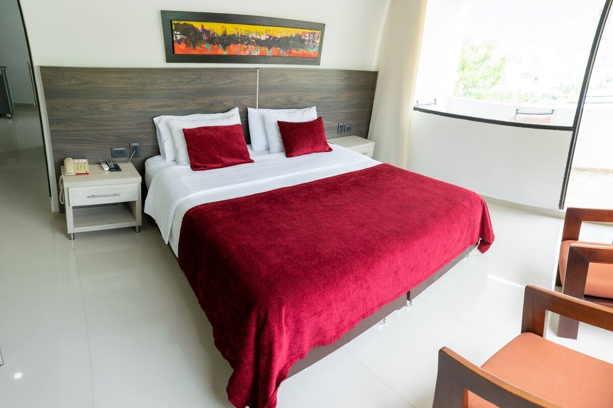 Een hotelkamer met een bed, nachtkastje, stoel en een schilderij aan de muur.