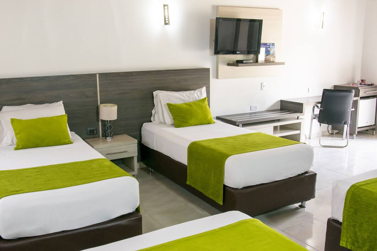 Een hotelkamer met twee bedden, een bureau, een stoel en een televisie aan de muur.