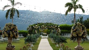 Eine Hochzeitslocation im Freien mit einem Blumenschmuckbogen, Palmen und Lichterketten.