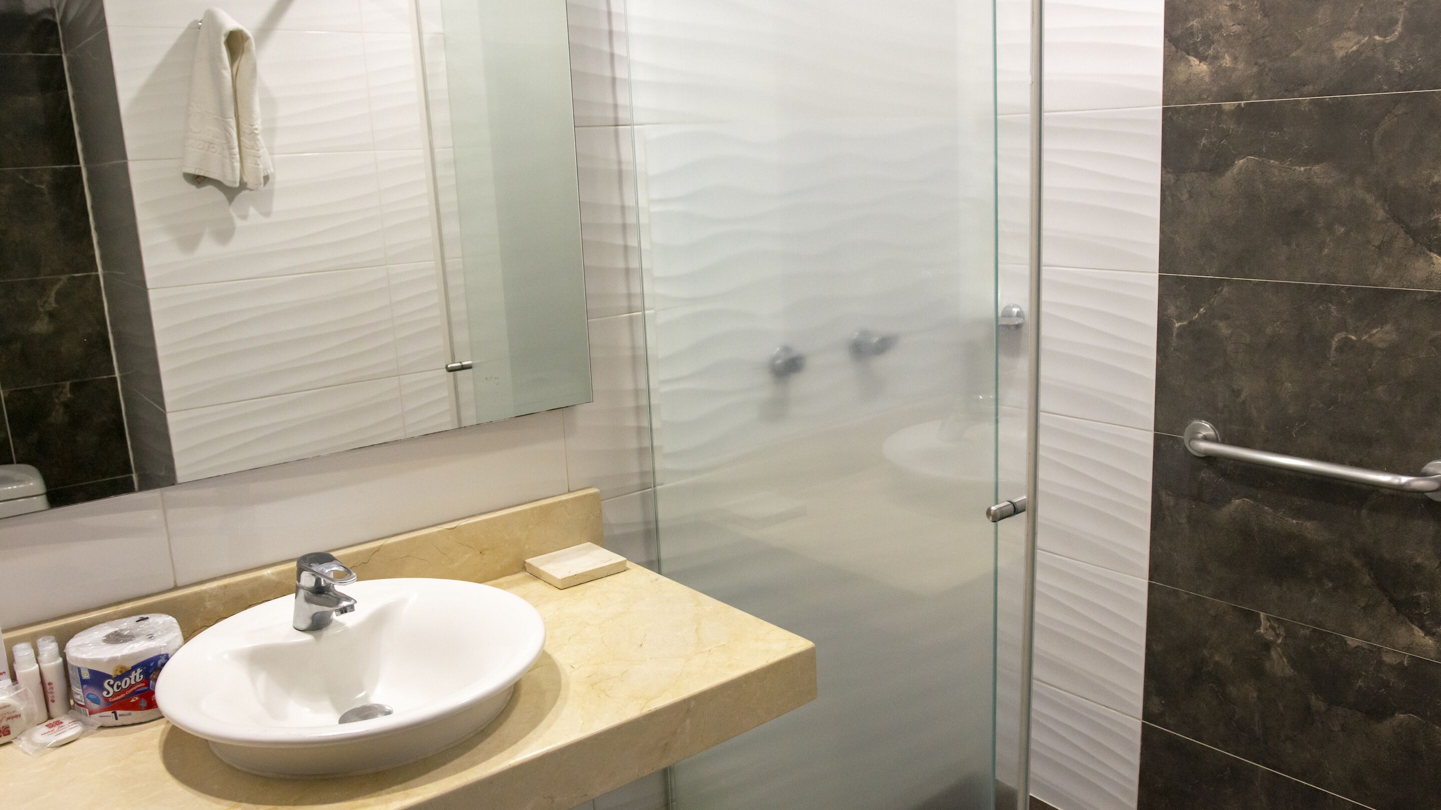 Un baño con un lavamanos blanco, cabina de ducha con vidrio y un espejo.