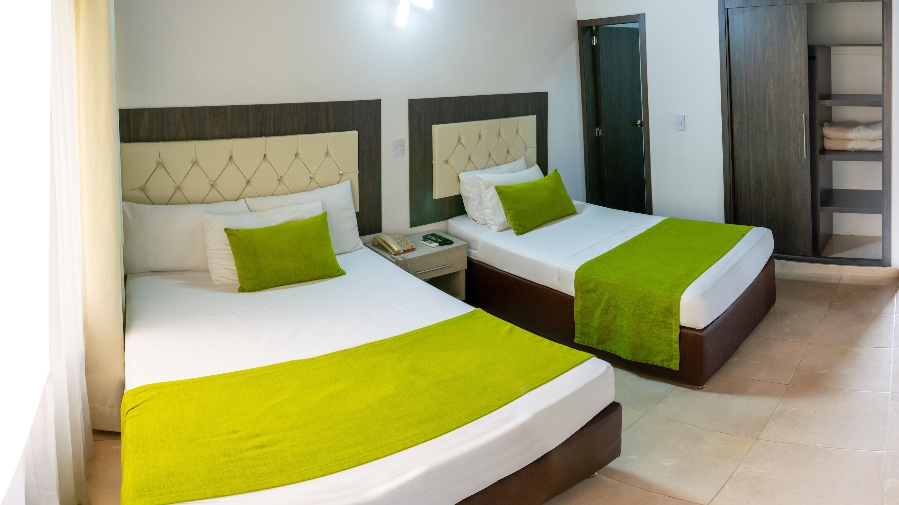 A hotel room with two beds, each with a green bedspread and matching pillows. There is a nightstand with a telephone and a book.