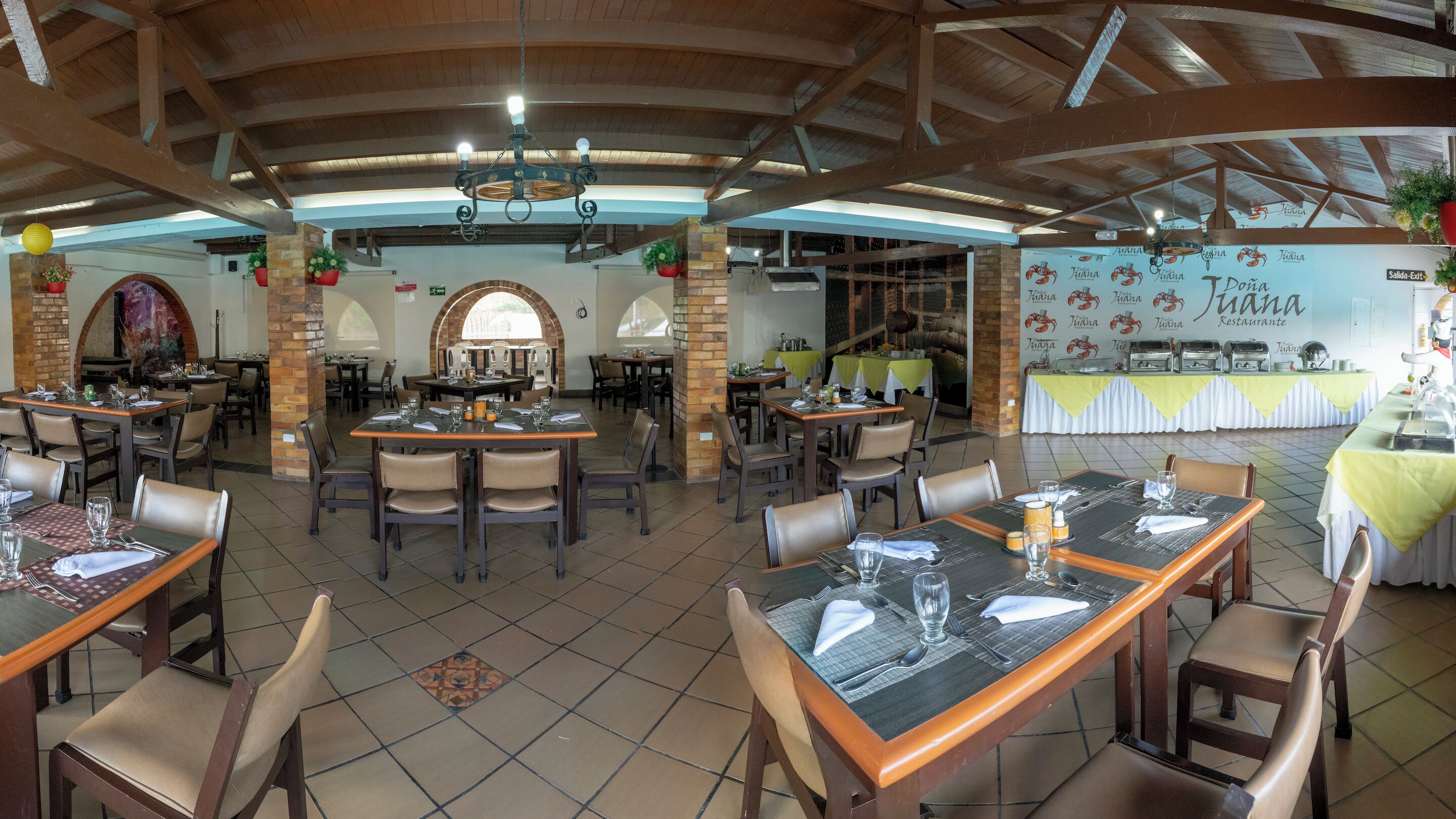 Un restaurante con varias mesas y sillas, una pared de ladrillo y un techo con vigas de madera.
