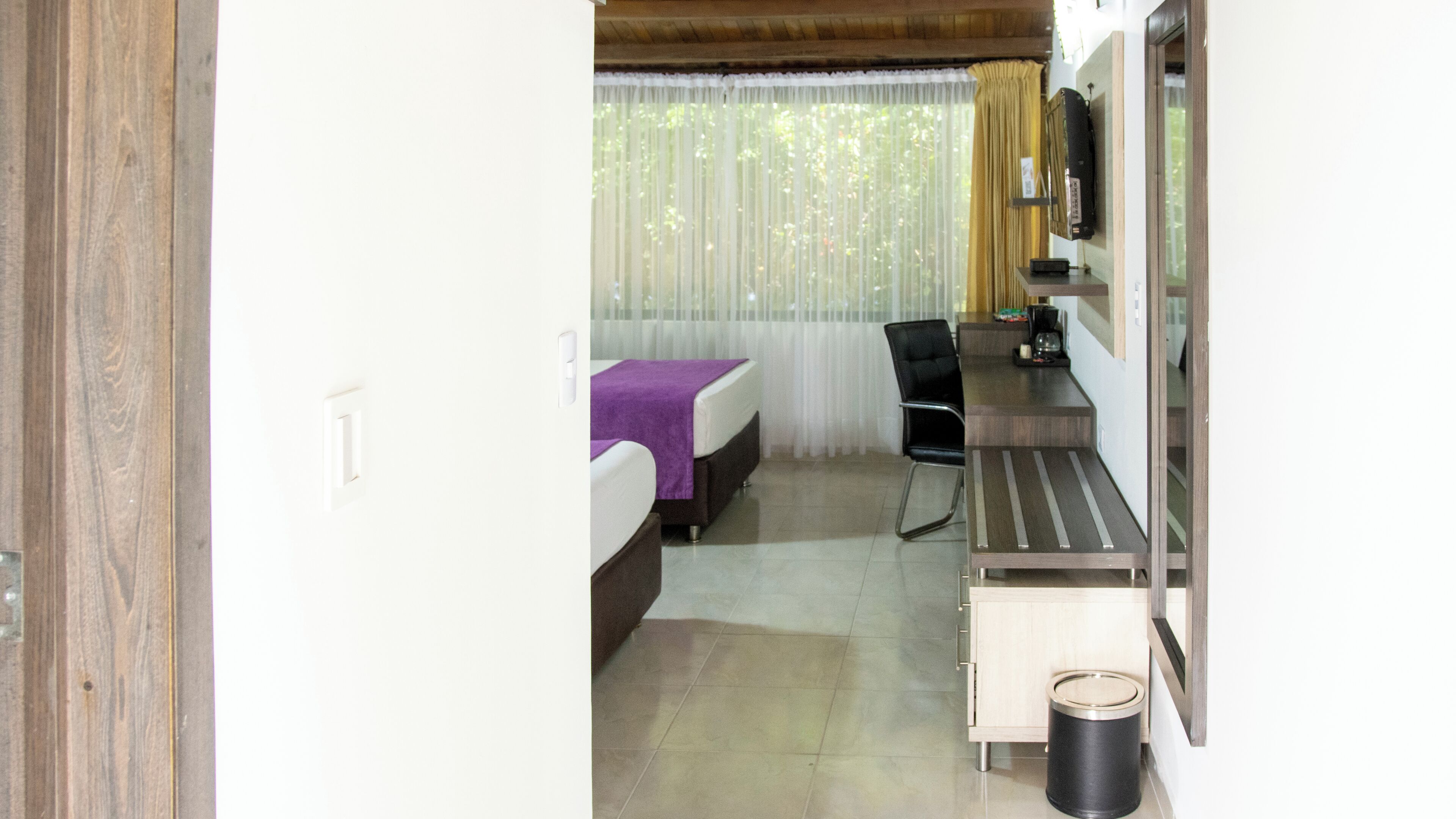 Una habitación de hotel con cama, escritorio, silla y cubo de basura.