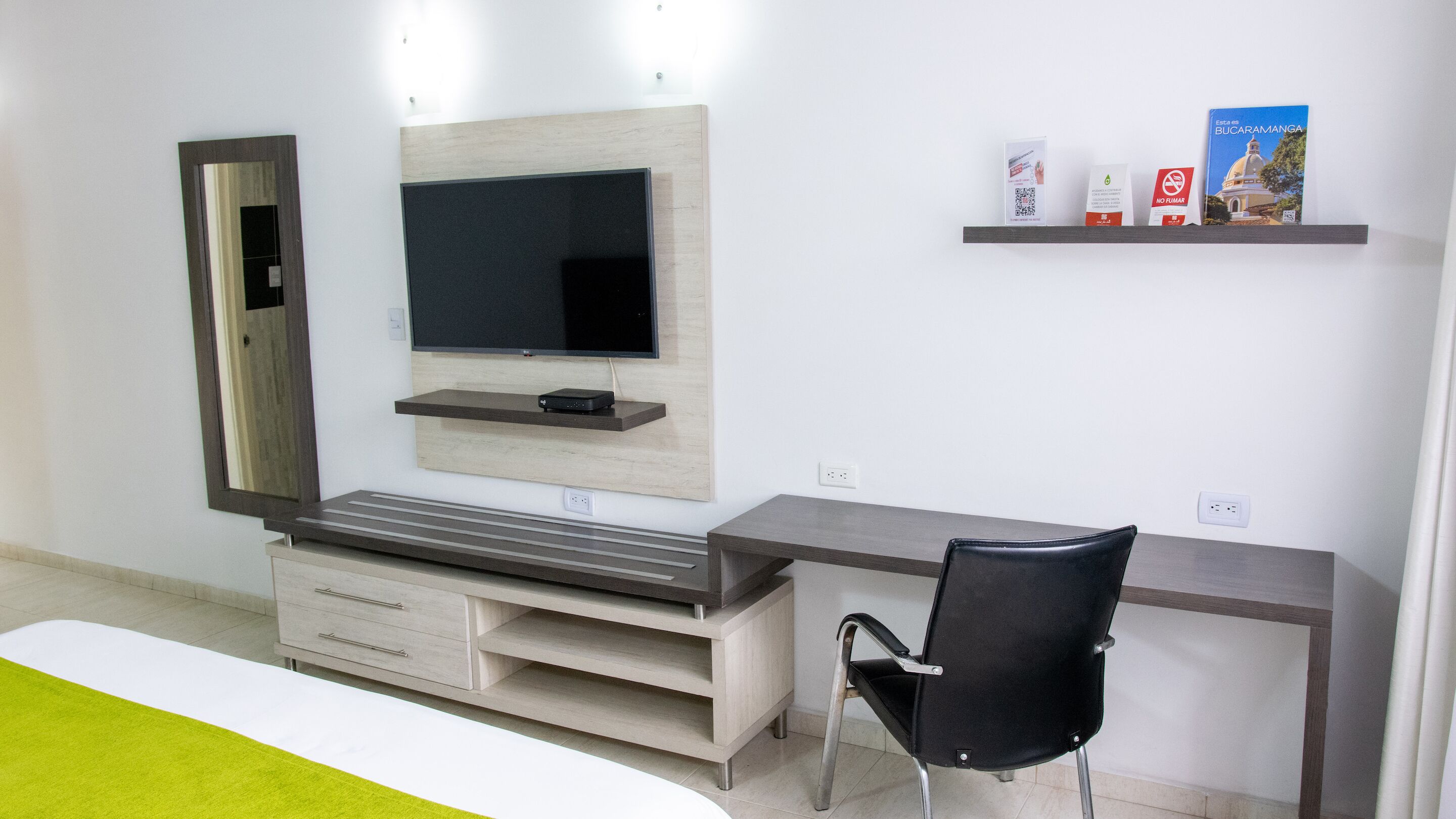 Un dormitorio moderno con cama, escritorio, silla, televisor y estante con libros y una caja.