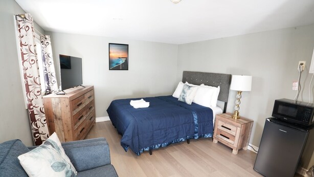 A bedroom with a bed, a dresser, a television, a microwave, and a refrigerator. - Falcon Inn (Niagara Falls)