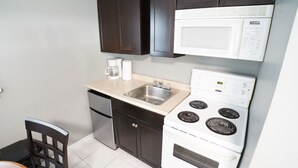 A compact kitchen with a microwave, stove, sink, and dark cabinets. - Falcon Inn (Niagara Falls)