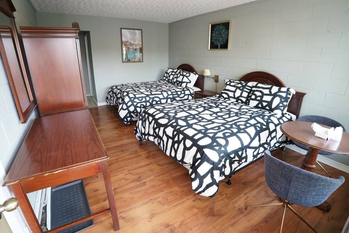 A hotel room with two beds, a wooden desk, a chair, and a small table.