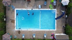 An aerial view of a rectangular swimming pool with a diving board, surrounded by lounge chairs and umbrellas. - Falcon Inn (Niagara Falls)