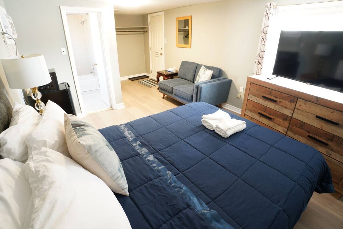 A hotel room with a bed, a chair, a TV, and a wooden dresser.