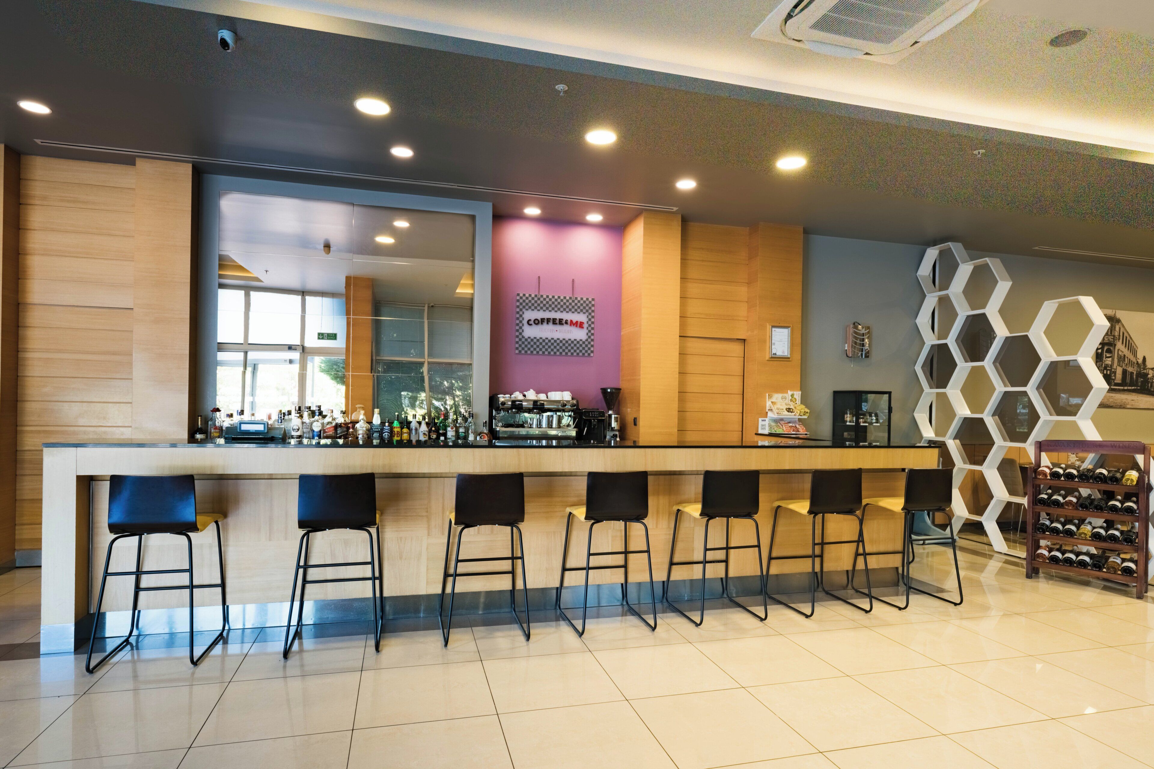 Un espace bar moderne doté d’un long comptoir, de plusieurs tabourets et d’une machine à café.