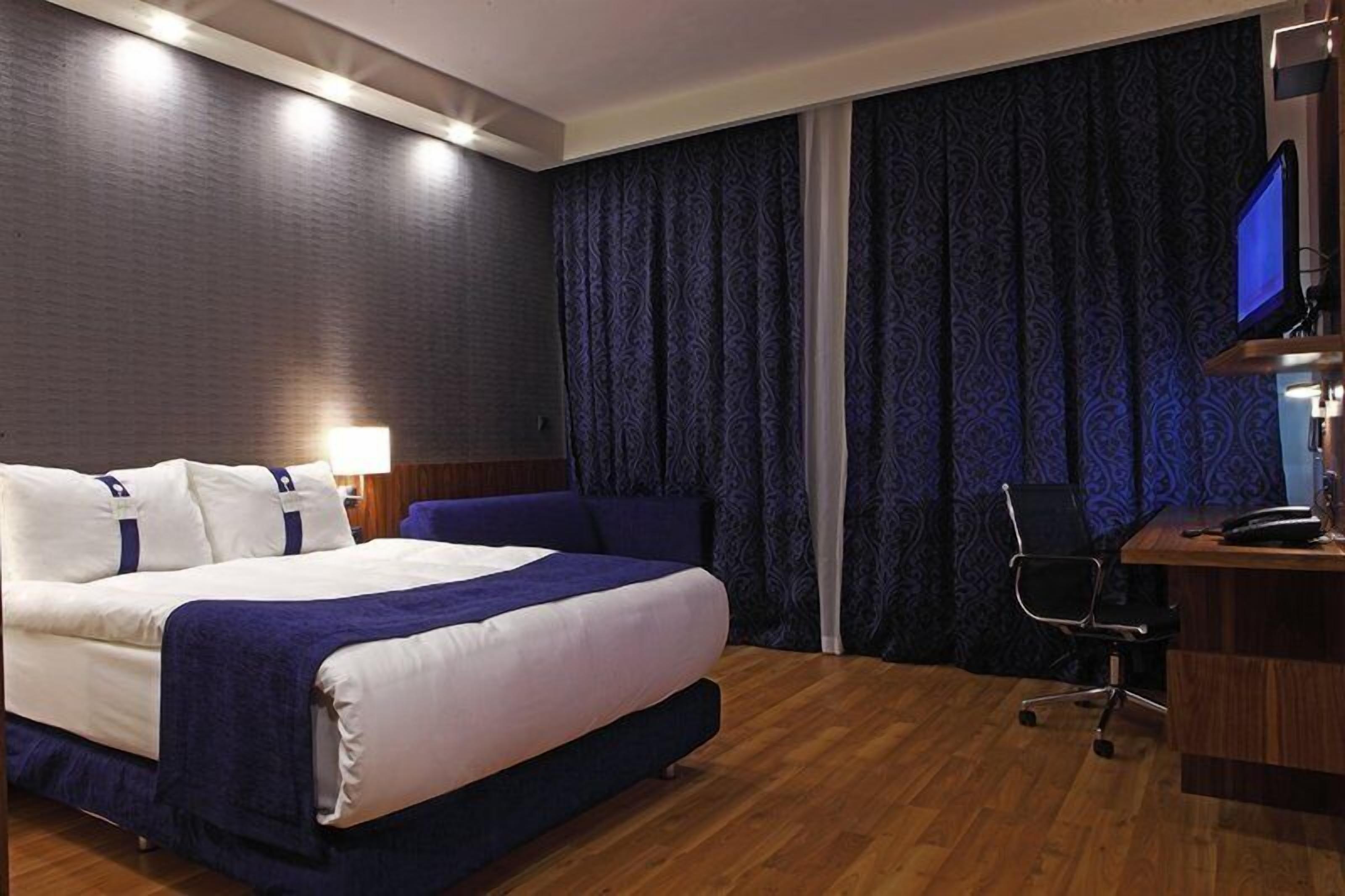 Habitación de hotel con cama, escritorio, silla, televisor y cortina.