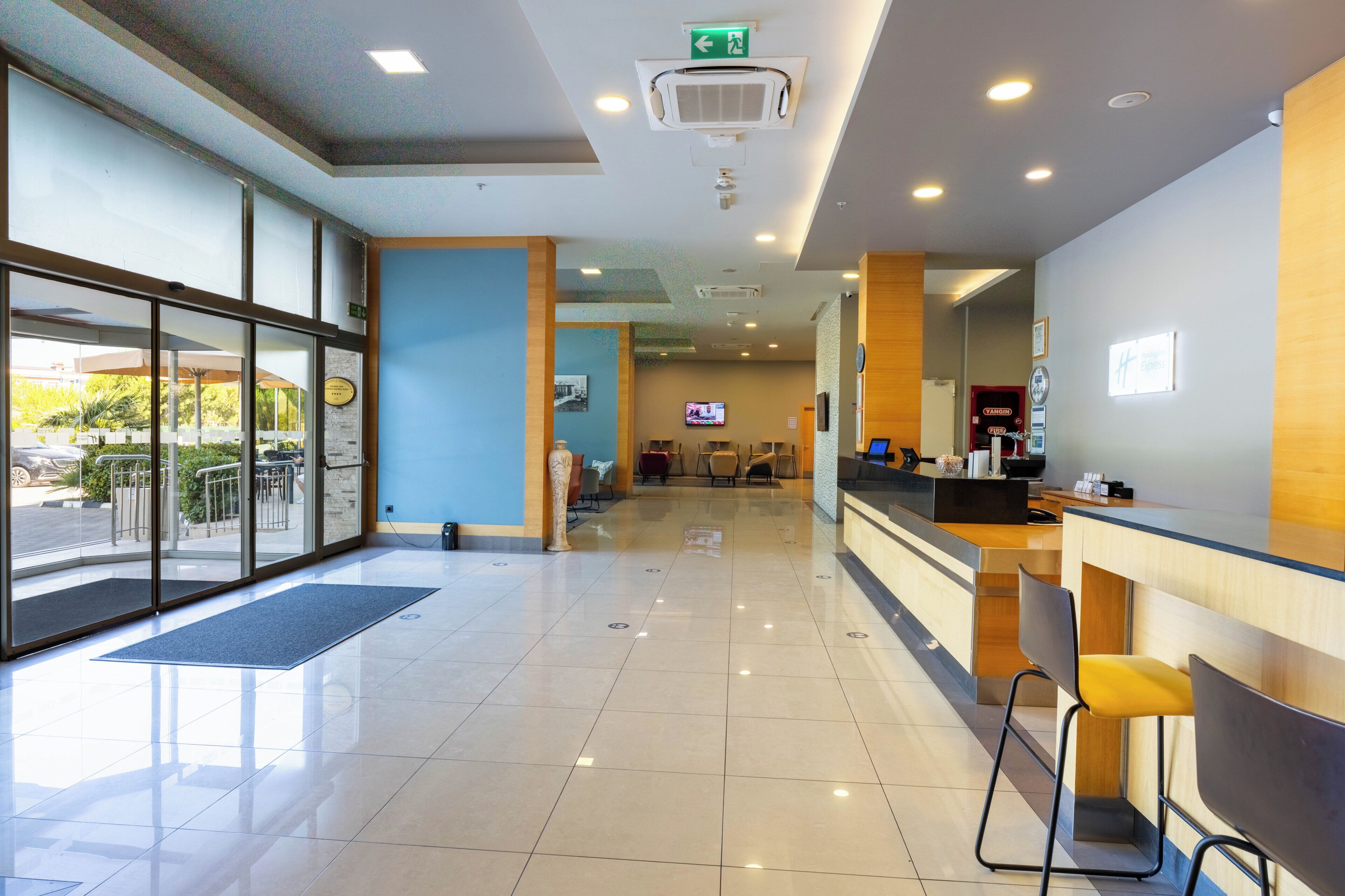 A hotel reception area with a glass entrance, a reception desk, and seating.